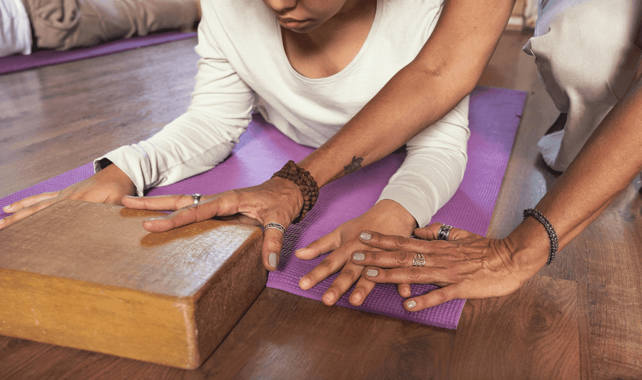 Image of a yoga teacher showing a student how to use a block for support in class