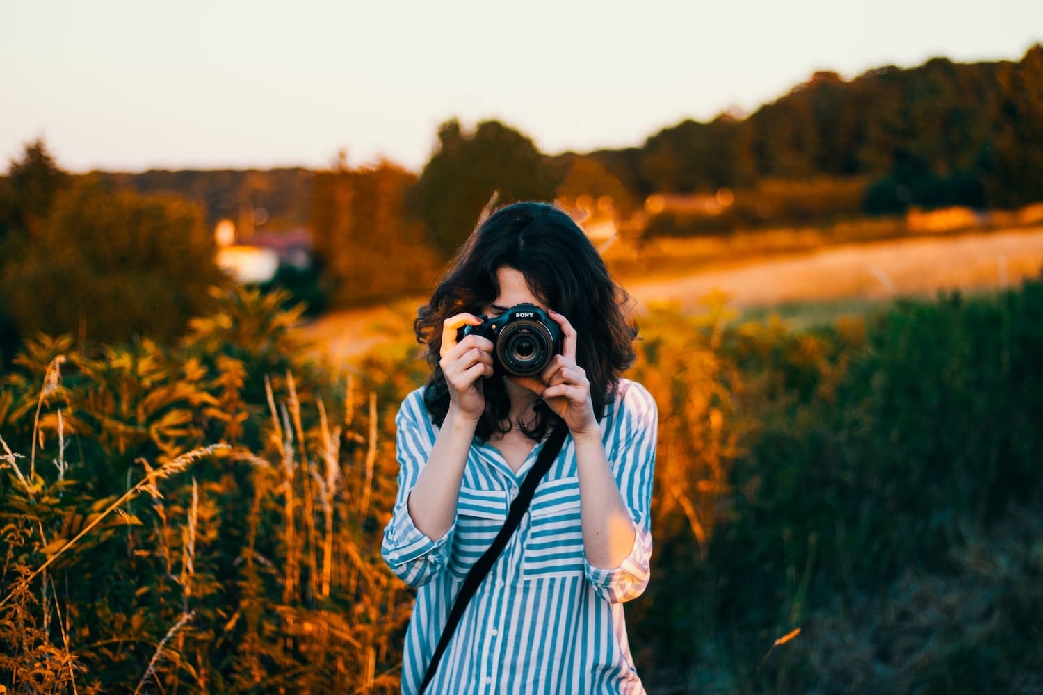 Woman facing camera with a camera. Blog about tips for taking professional yoga and fitness photos.