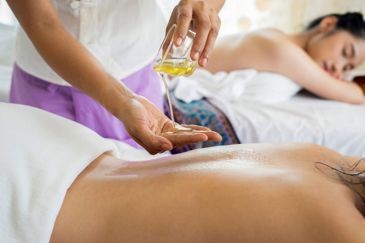 a massage therapist applying oils to the back of a client before massaging