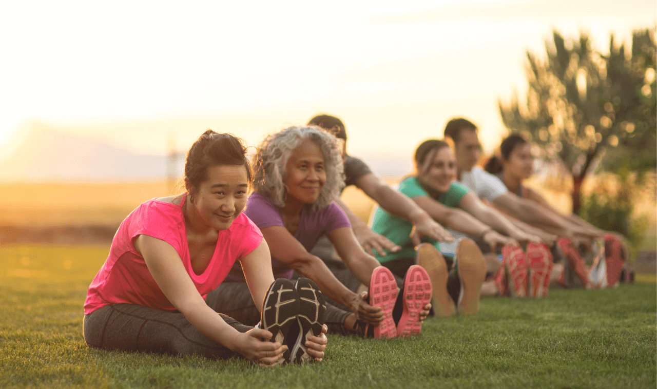 People doing yoga on green grass in front of a field on a sunny day