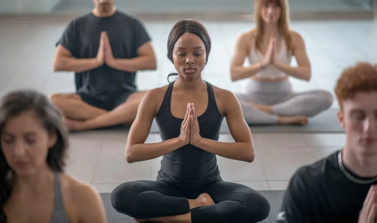 Woman sitting in lotus pose | OfferingTree A young woman sitting in lotus pose in a larger yoga class