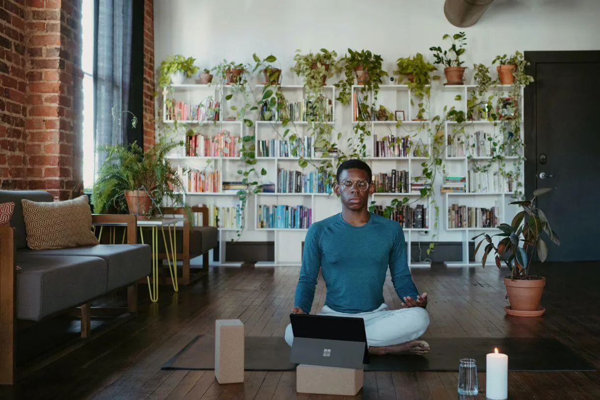 Man sitting in his apartment with lots of plants in the background doing yoga online