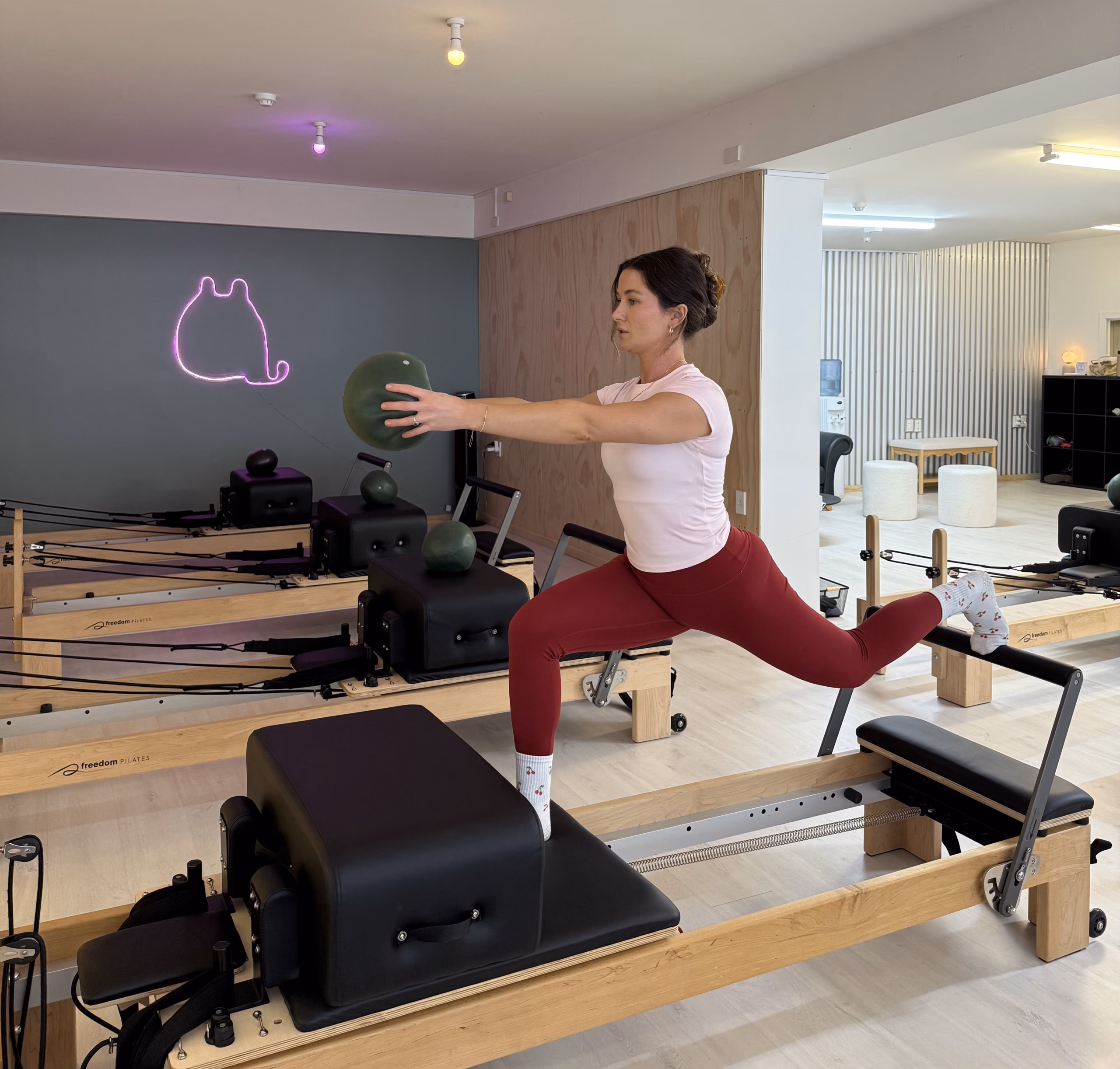 IMG_4364 Pilates reformer studio with multiple reformer machines in a bright room, mirrors, and string lights along the wall
